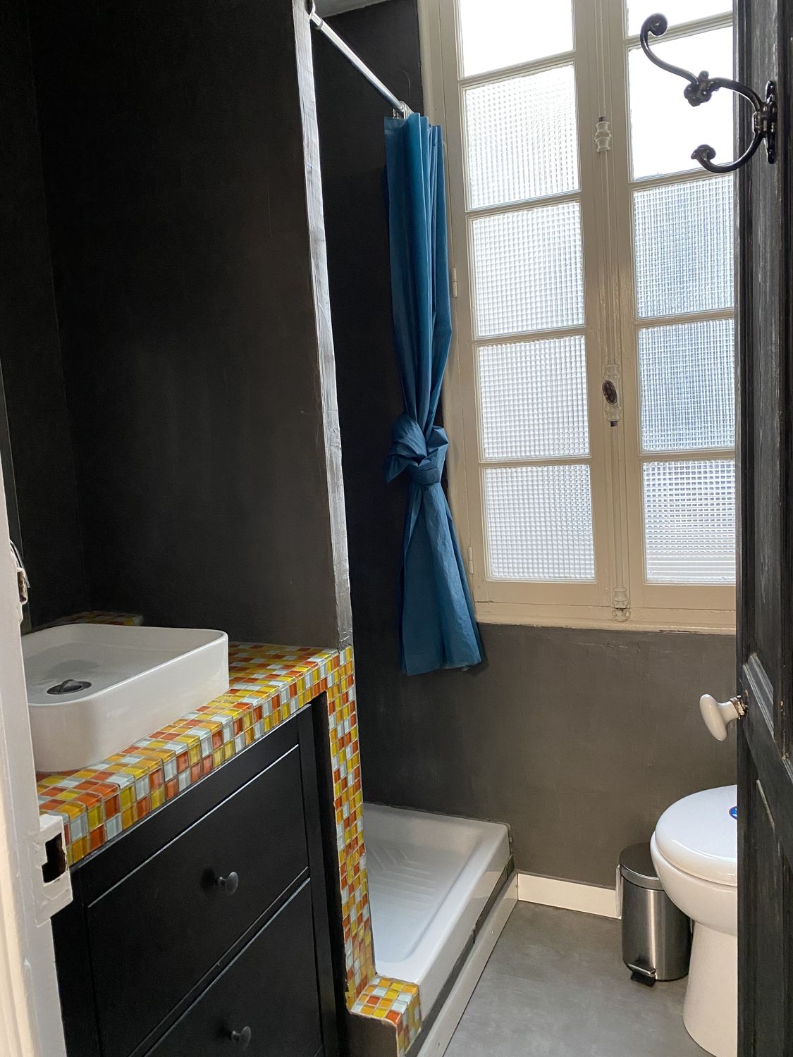 Petite salle d'eau avec douche, rideau bleu et plan de vasque en mosaïque orange