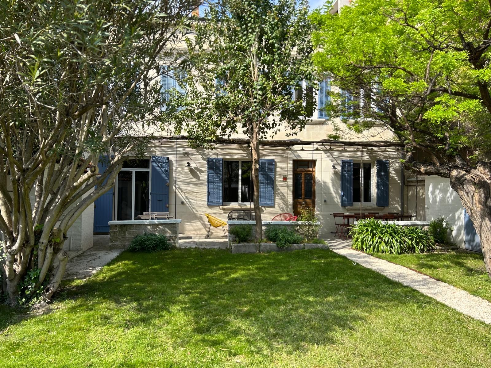 Façade de la maison aux volets bleus vue depuis le jardin arboré