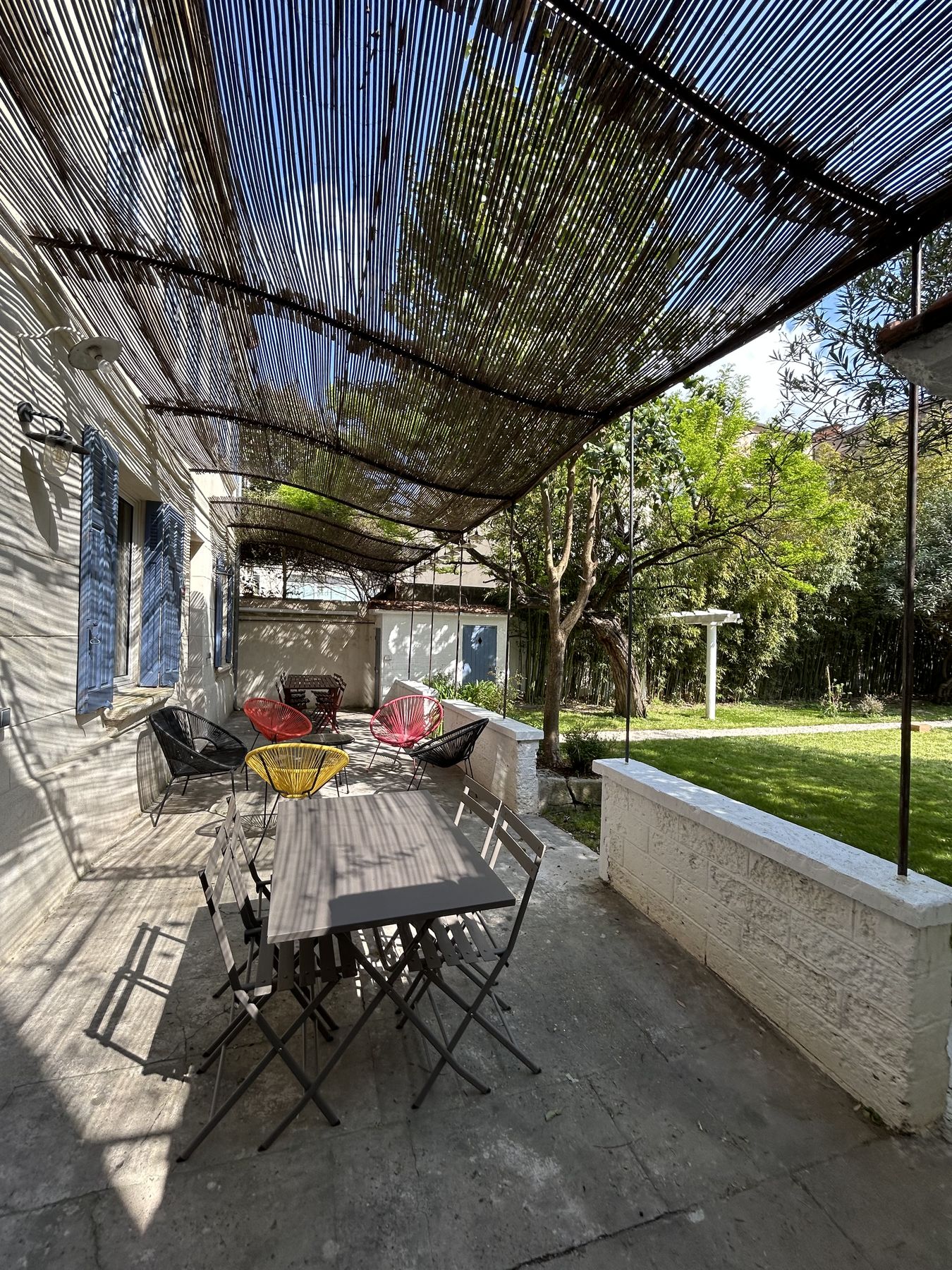 Terrasse ombragée sous une pergola de canisse avec table et fauteuils Acapulco colorés